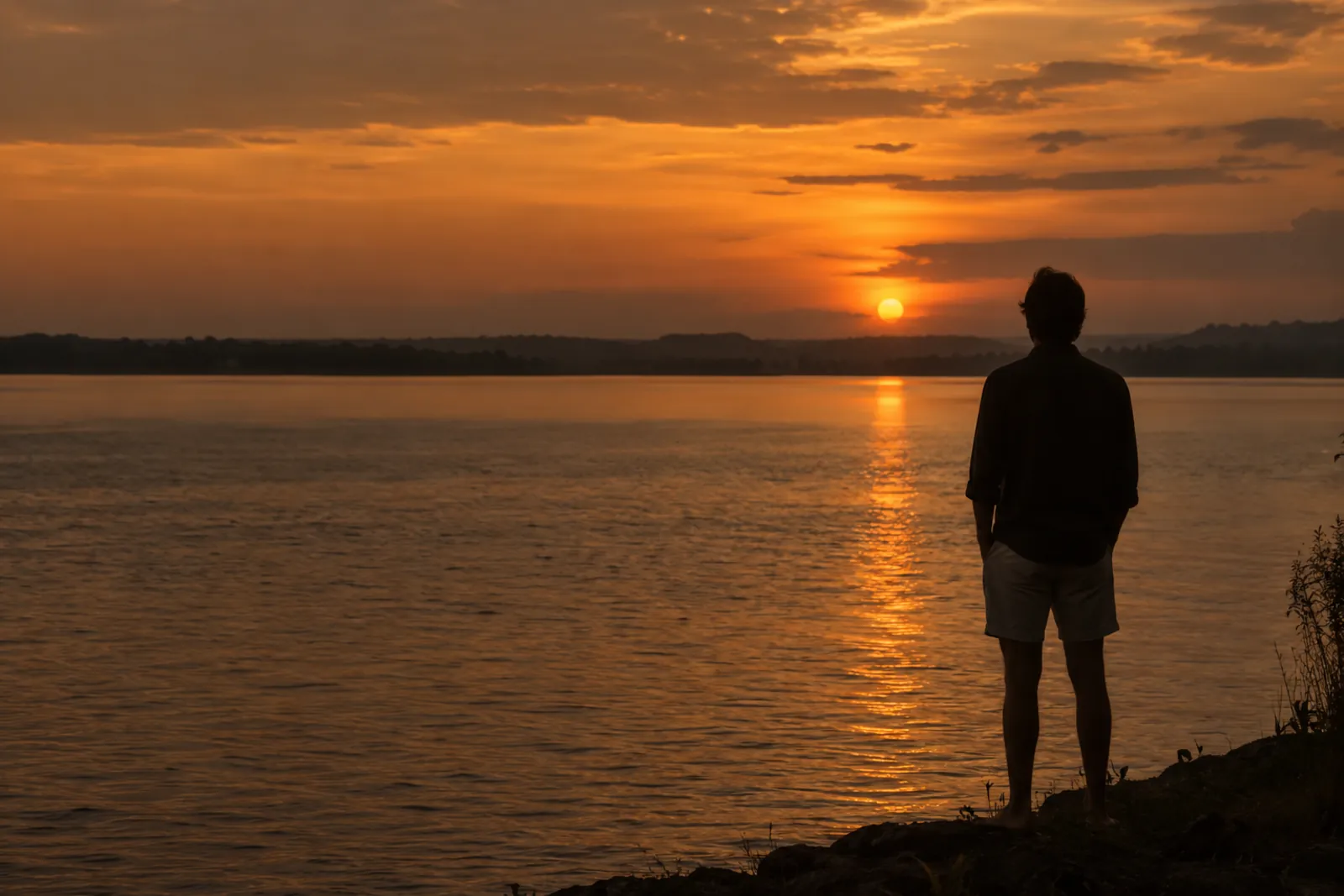 A lone figure standing on the shore, watching the sun go down over the water